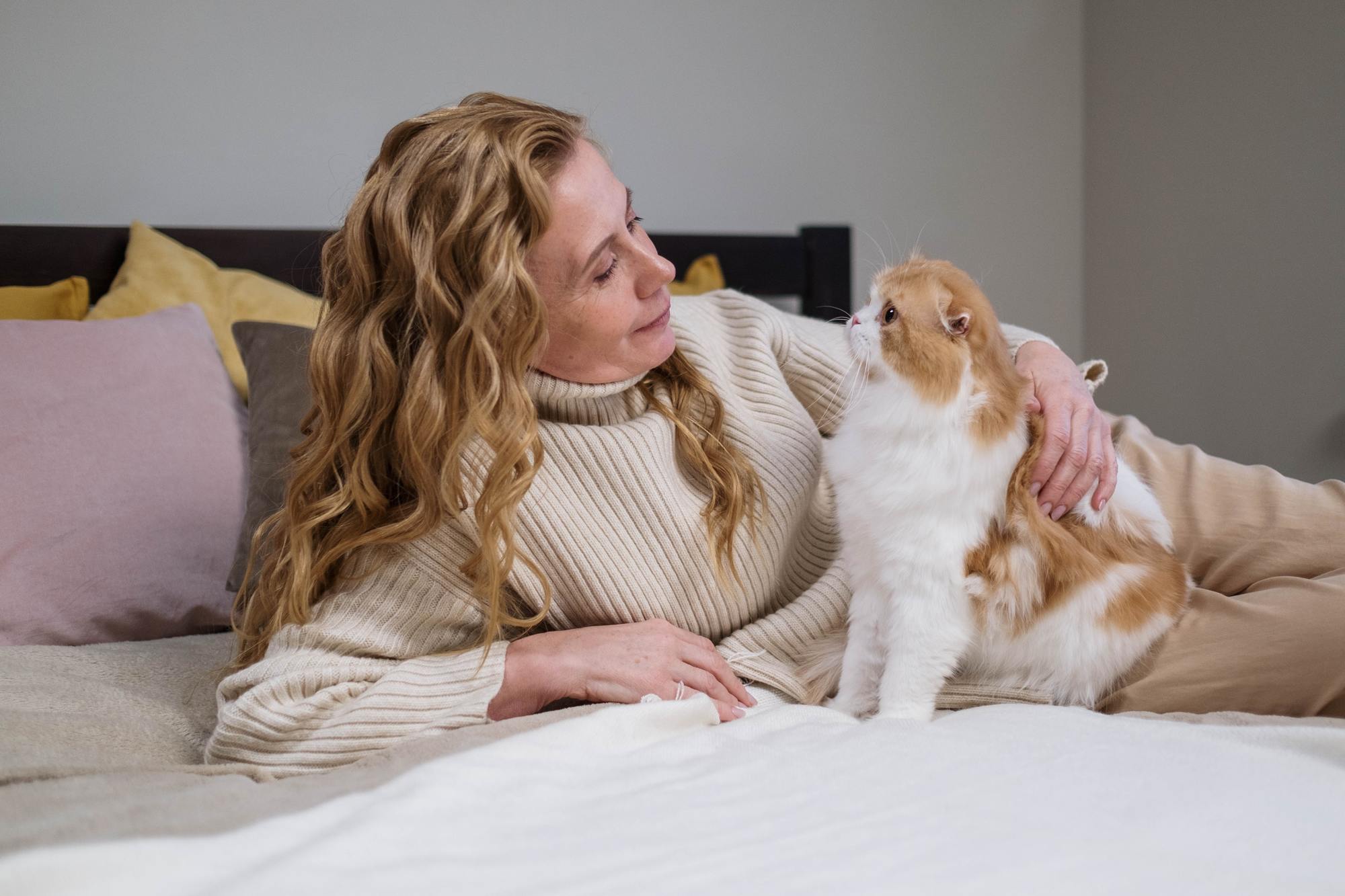 Woman sat on a bed with a white and ginger cat